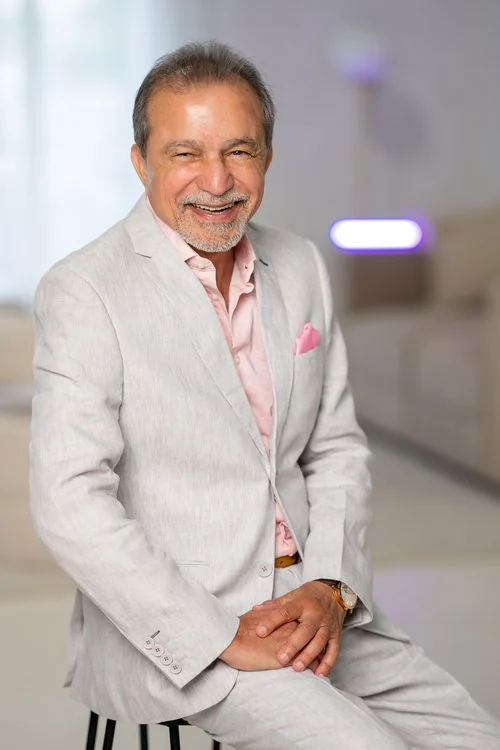 Abid Iftikhar laughing, seated in a light linen suit