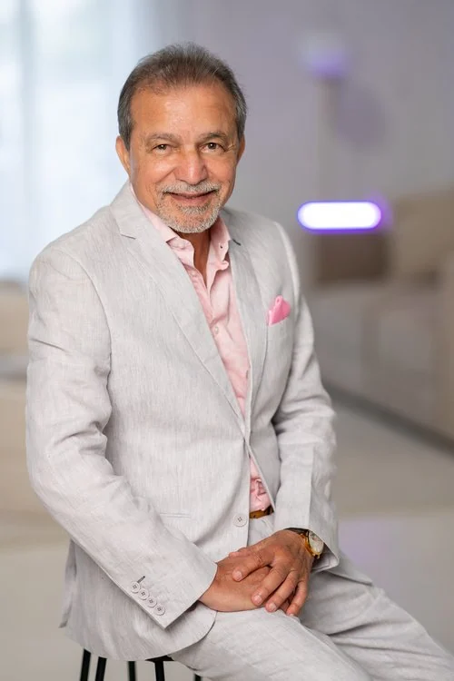 Abid Iftikhar seated in a light linen suit, smiling